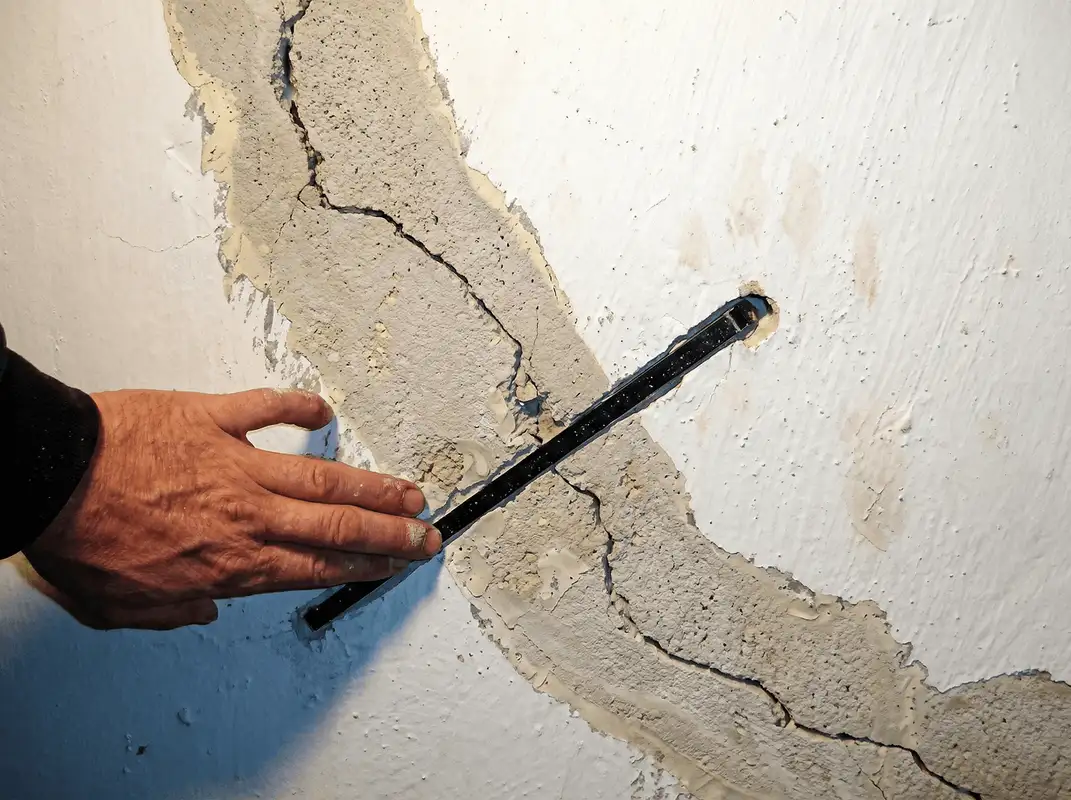 A wall with a large crack is being inspected by a professional in Des Moines, IA